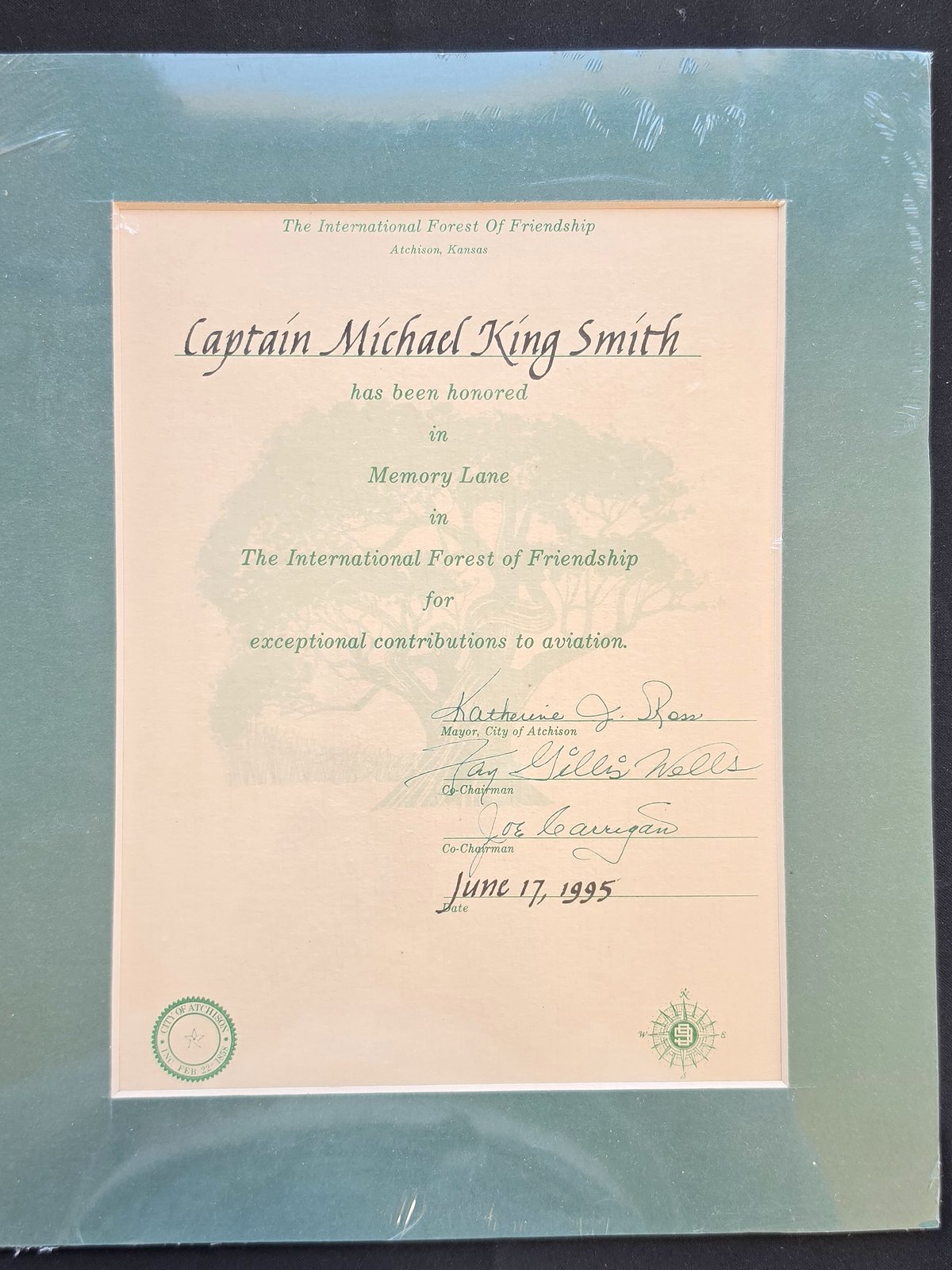 Certificate from The International Forest of Friendship, Atchison, Kansas, stating that Captain Michael King Smith has been honored in Memory Lane for exceptional contributions to aviation, dated June 17, 1995, in a green mat