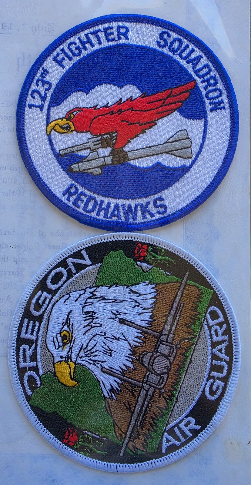 Two embroidered patches in a binder sleeve: 123rd Fighter Squadron Redhawks, with a red hawk carrying a missile, and Oregon Air Guard, with an eagle's head and a fighter jet
