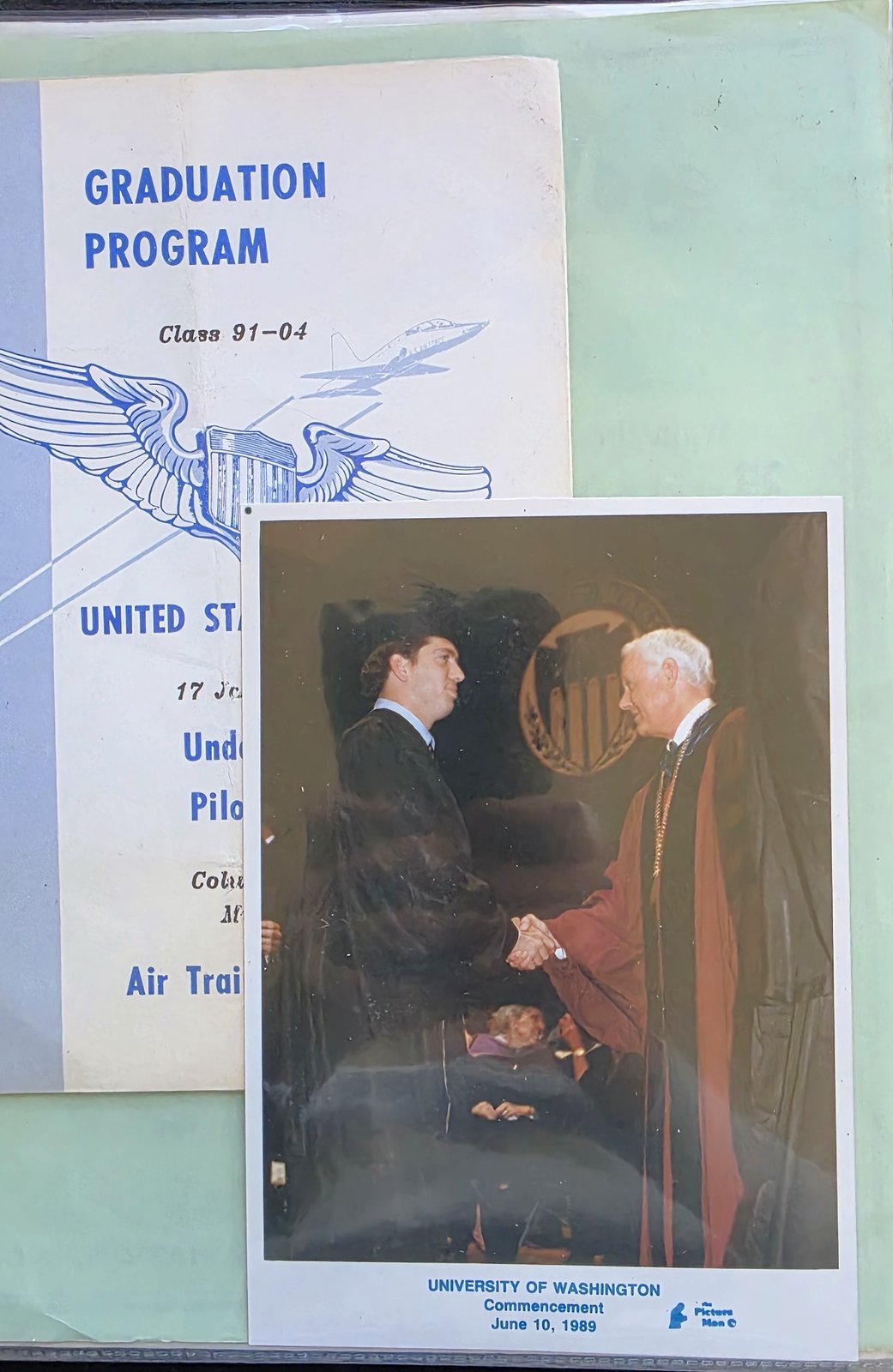 Binder page holding a United States Air Force Undergraduate Pilot Training graduation program for Class 91-04, partly covered by a University of Washington commencement photo card dated June 10, 1989, showing Michael in a gown shaking hands with an official in academic robes